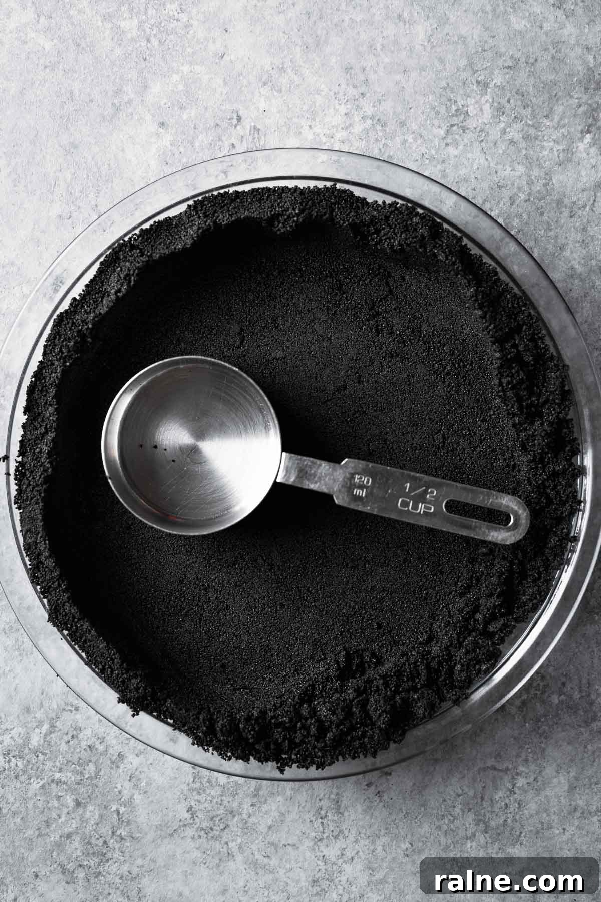 Chocolate Cookie Crust Recipe for Perfect Pie and Cheesecake 8 Cookie crumbs being pressed into a pan with a measuring cup.