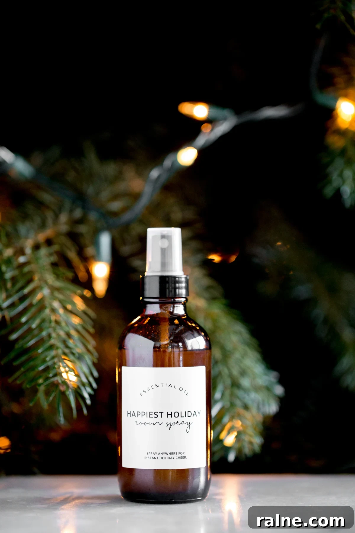 bottle of homemade DIY essential oil holiday room spray with a lit tree in the background title text overlay