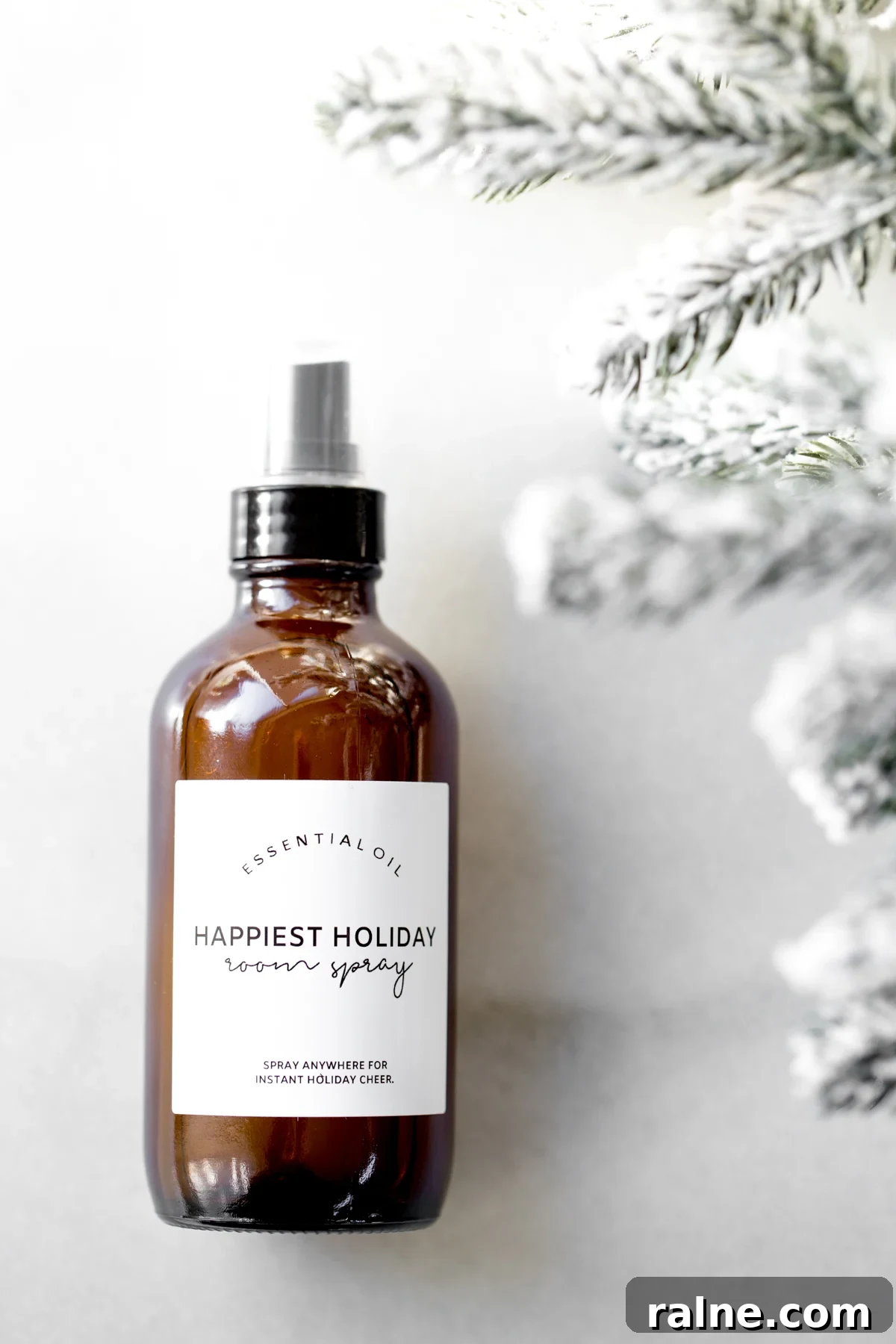 Bottle of holiday room spray on marble background with snow covered tree branches on the side