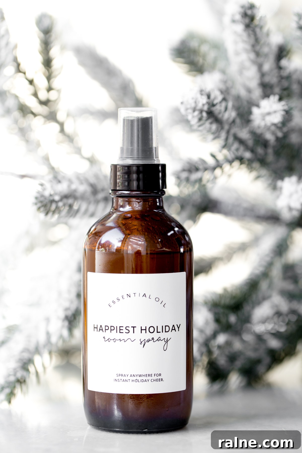 Homemade essential oil Christmas room spray on marble with snow covered tree branches in the background
