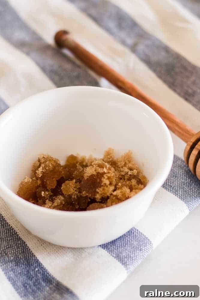 Brown sugar scalp scrub in white bowl with wooden honey dipper.