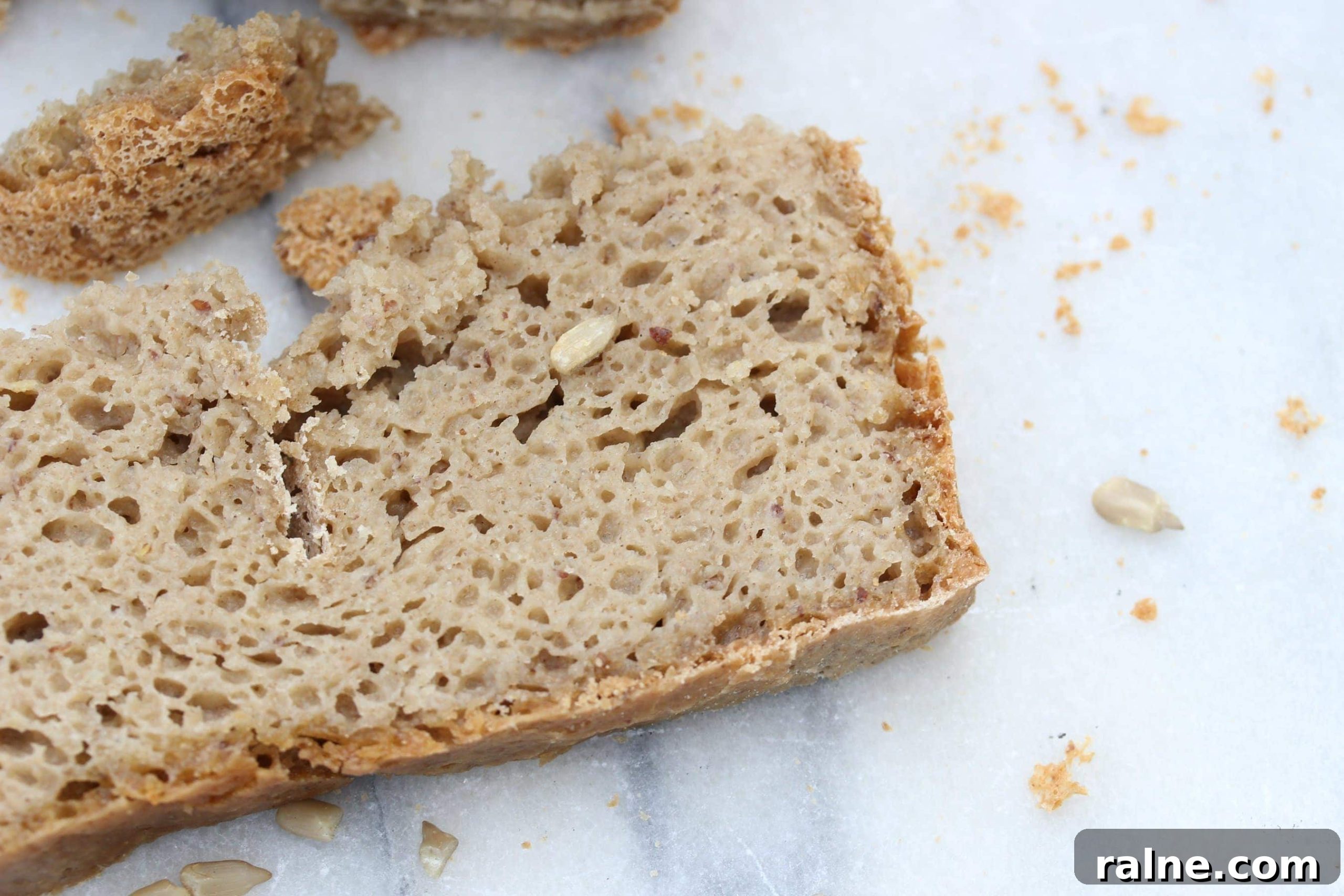 Gluten-Free Vegan Bread Machine Recipe: Soft Loaf Guide 6 A cut slice of bread laying flat on a marble board. There are crumbs scattered around. You can see the soft texture of the light brown bread and some of the seeds inside.