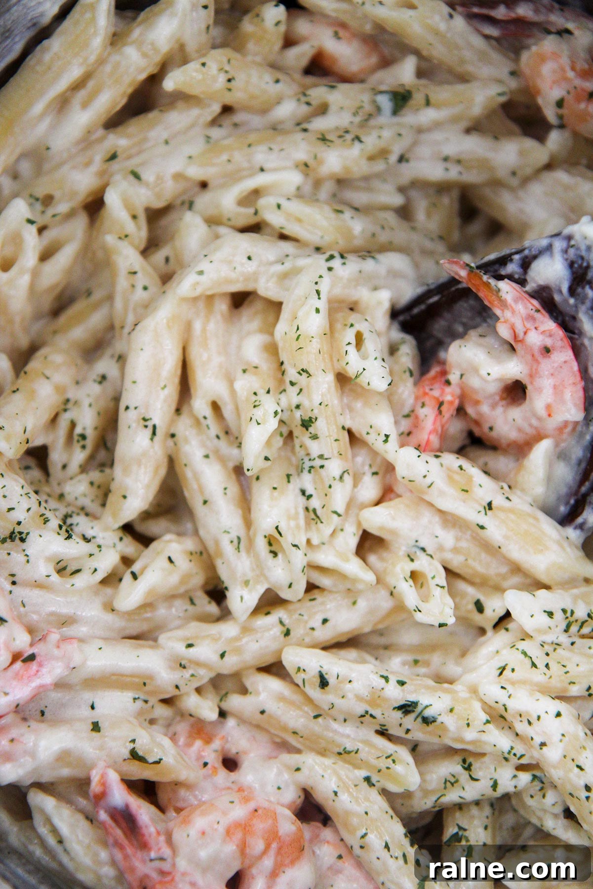 Shrimp and pasta covered in sauce with parsley and a wooden spoon up close.