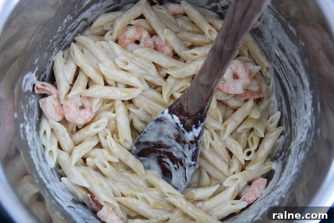 Shrimp alfredo penne pasta with a wooden spoon in the instant pot.