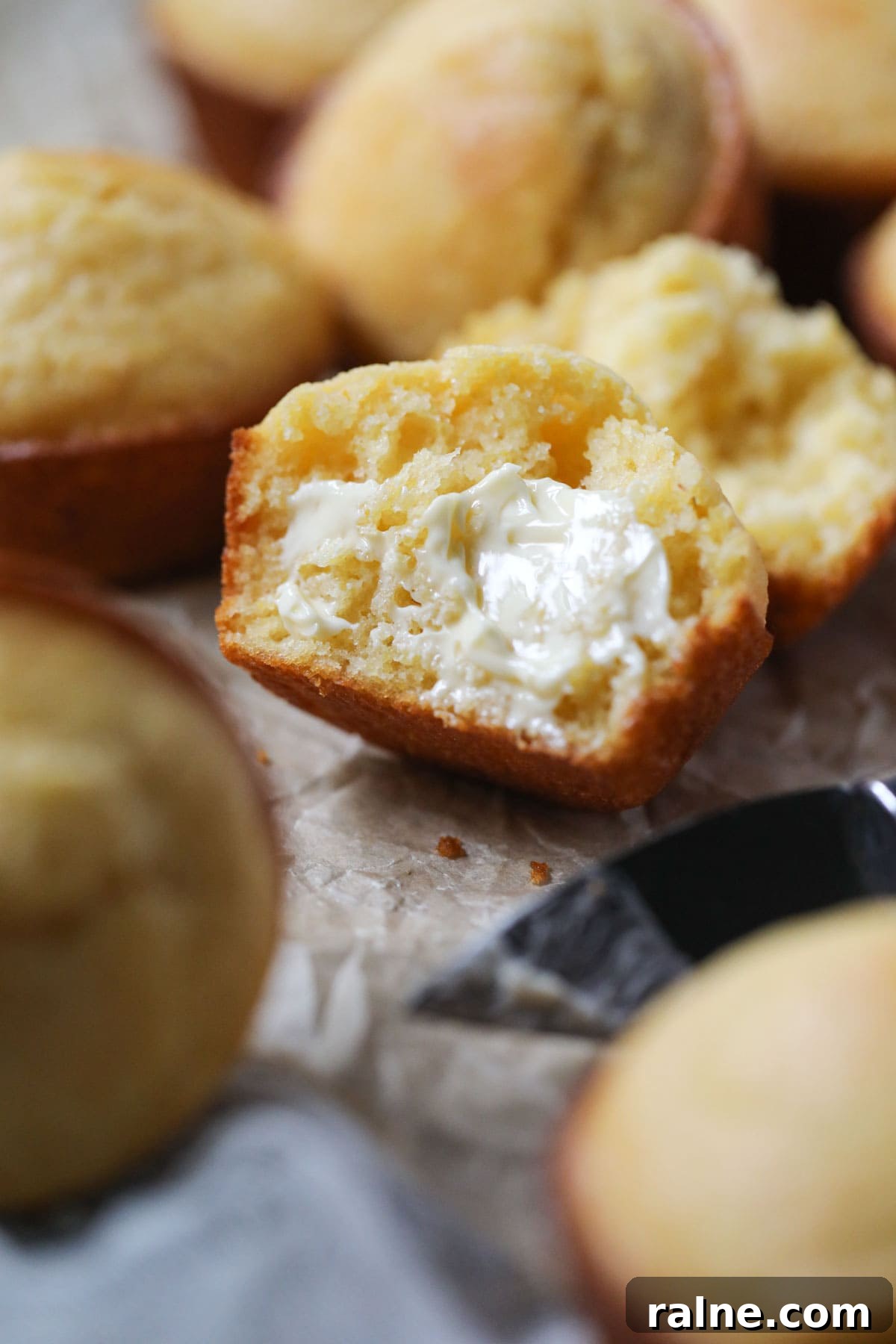 buttermilk cornbread muffin sliced open to show texture on parchment paper.