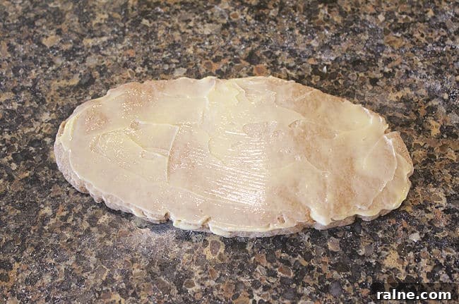 Single-Serve Blueberry Cinnamon Roll Recipe 8 Dough spread with butter on a granite counter.
