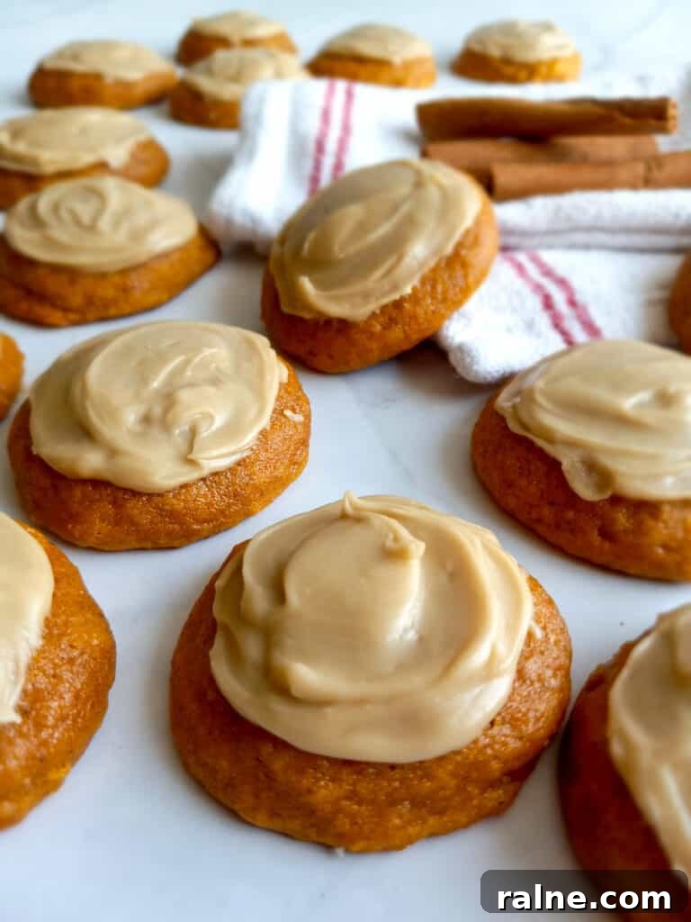 pumpkin cookies with caramel frosting scattered around, with a towel and cinnamon sticks for decor