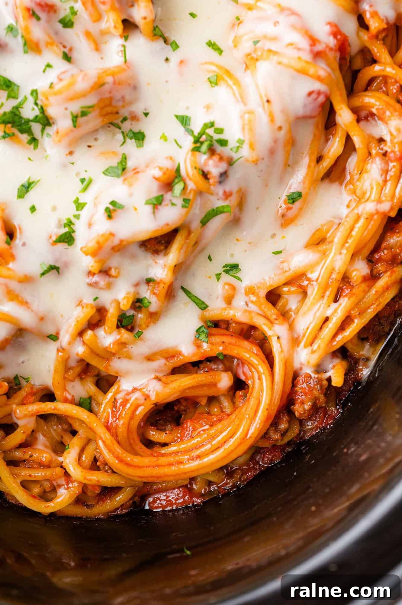 Slow-Cooker Spaghetti with Savory Meat Sauce 2 Close-up of spaghetti topped with melted cheese and garnished with chopped parsley.
