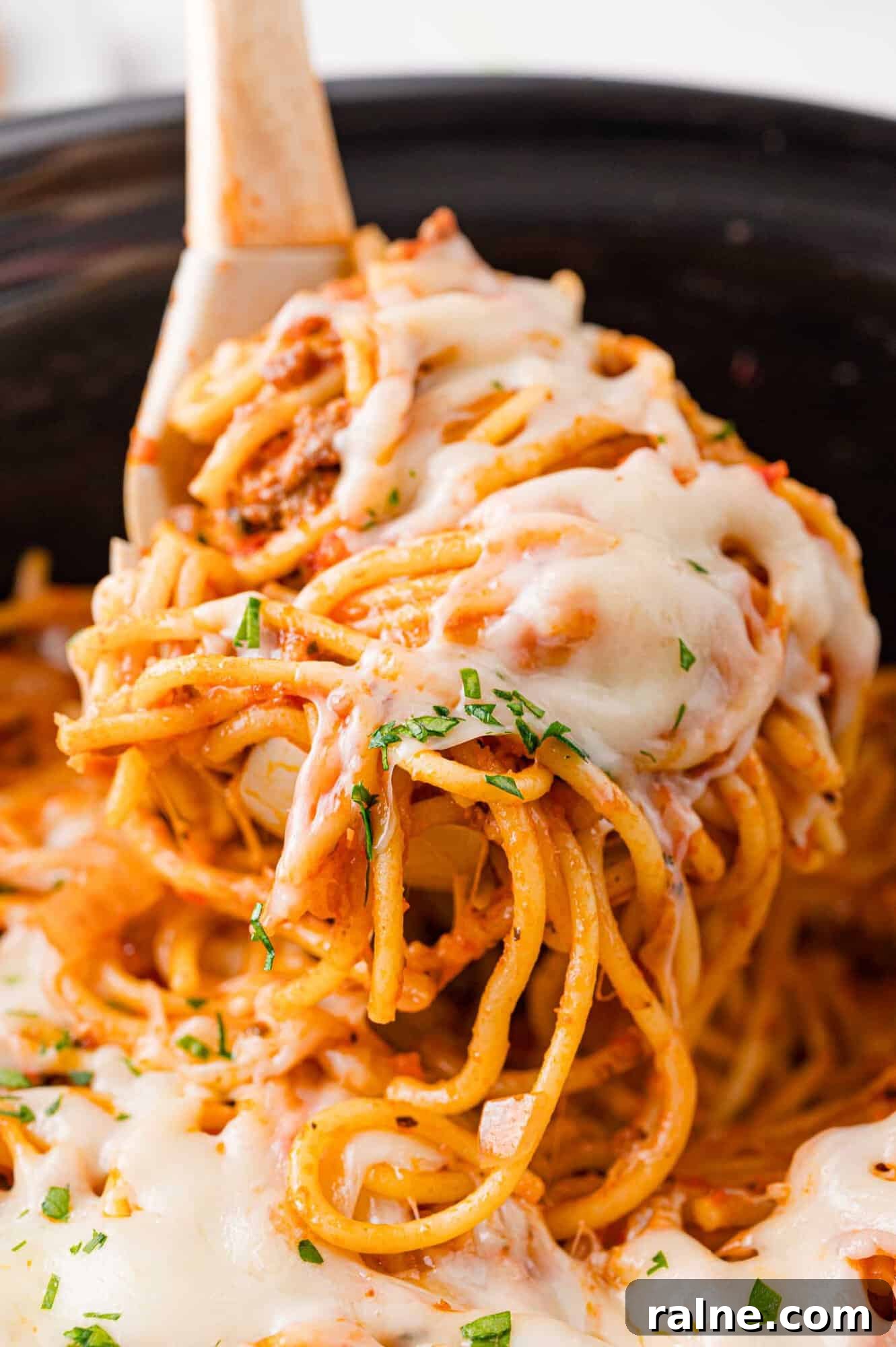 Slow-Cooker Spaghetti with Savory Meat Sauce 5 Close-up of cheesy spaghetti being lifted from a slow cooker, topped with melted cheese and parsley.