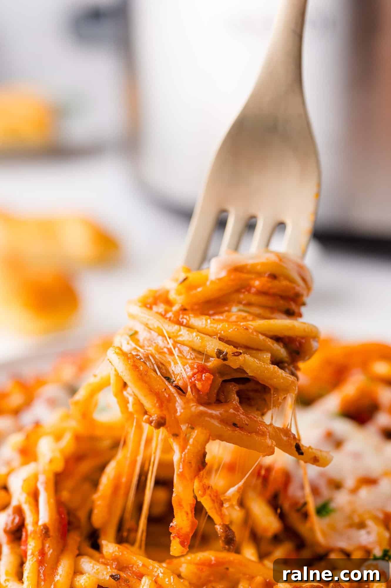 Slow-Cooker Spaghetti with Savory Meat Sauce 3 Fork lifting a portion of spaghetti with tomato sauce, cheese, and herbs, with cheese strands stretching from the plate.