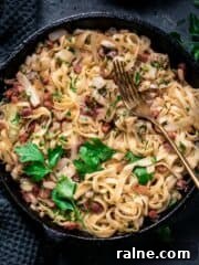 Fried cabbage and noodles with bacon in a skillet with fork.