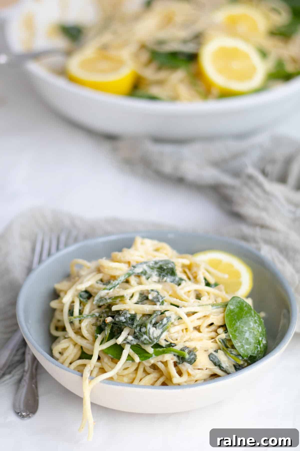 spaghetti with spinach and artichokes in a bowl with the pan behind it.