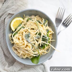 spinach artichoke spaghetti with a lemon in a bowl with forks next to it.
