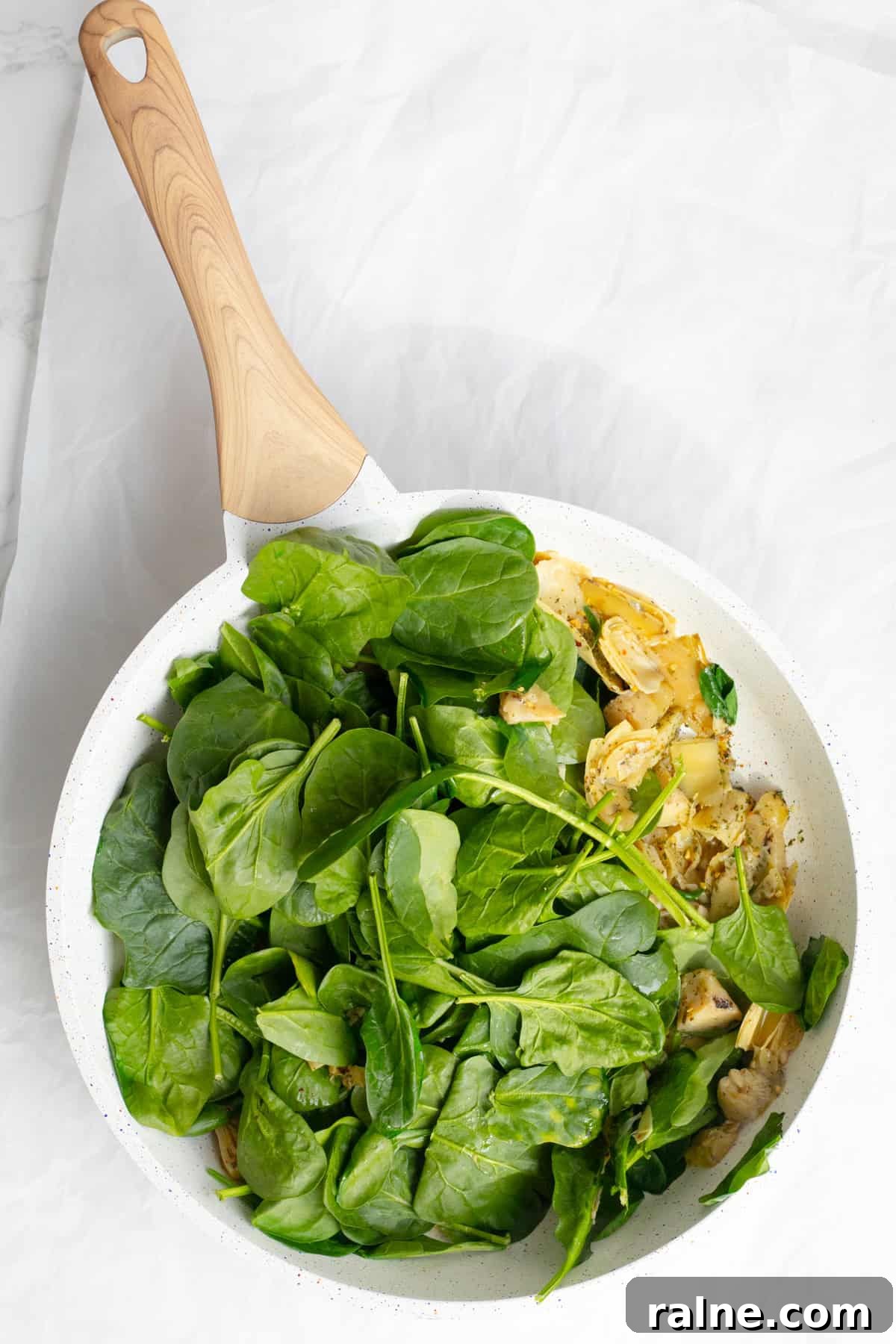 spinach cooking in a frying pan with artichokes
