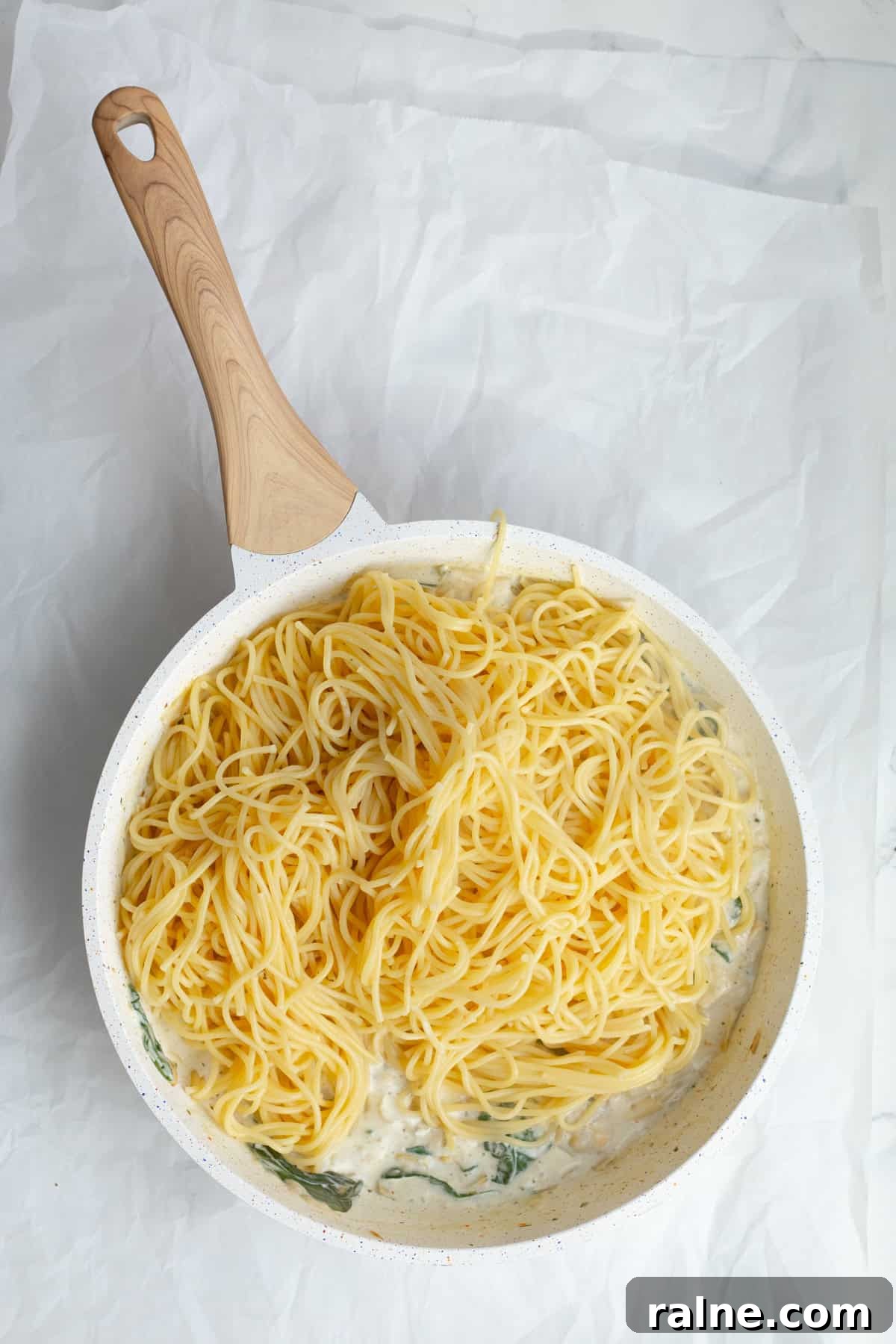 spaghetti noodles being added to sauce in a pan