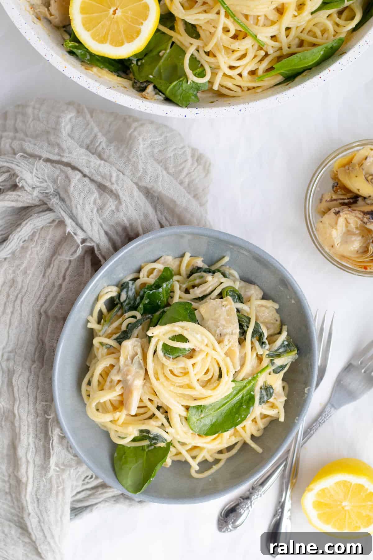 spaghetti with spinach and artichokes in a bowl with the pan behind it.