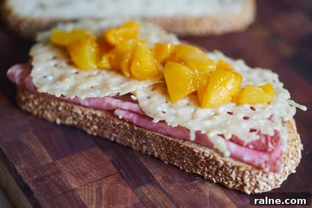 Salami Sandwich with Parmesan Crisps and Zesty Mostarda 2 An open-faced salami sandwich topped with frico and mostarda on a wooden cutting board.