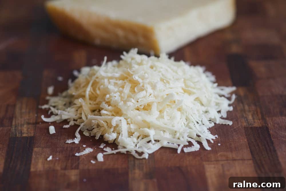 Salami Sandwich with Parmesan Crisps and Zesty Mostarda 3 Shredded parmigialno reggiano sits in the foreground on a wooden cutting board, with a block of the cheese in the background.
