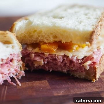 Salami Sandwich with Parmesan Crisps and Zesty Mostarda 7 A salami sandwich with parmesan cheese and mostarda cut in half on a cutting board.