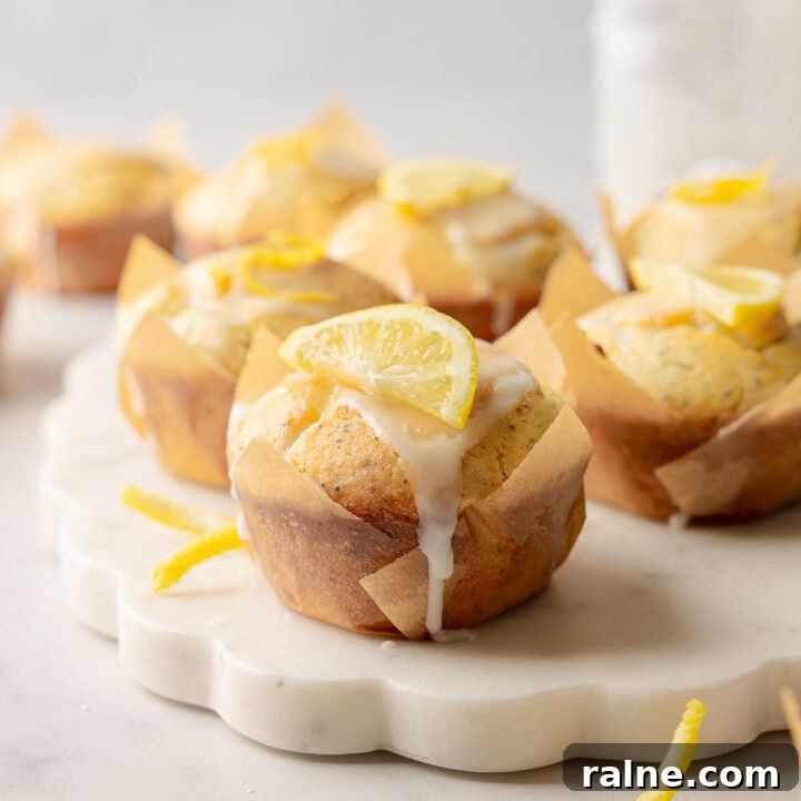 Lemon poppy seed muffins with glaze and lemon slice garnish on marble board.