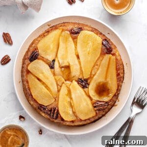 Top view of pear upside down cake on a white plate. Pecans, coffee cups, silver forks. Whitish background.