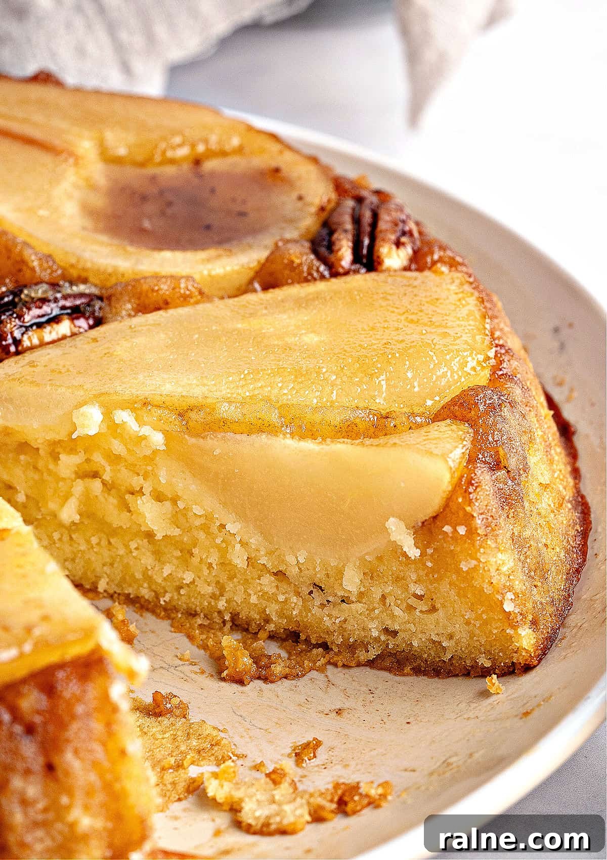 Close up slice of pear upside down cake on a cream-colored plate.