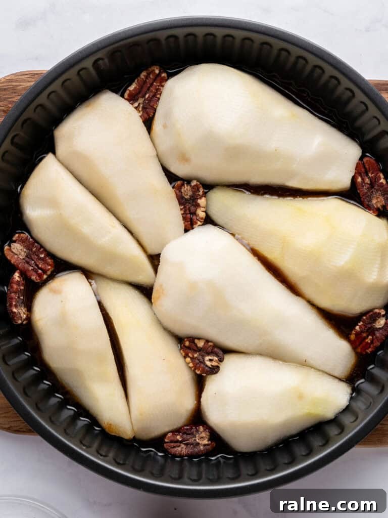 Several pear halves on top of caramel in a black cake pan. Top view.