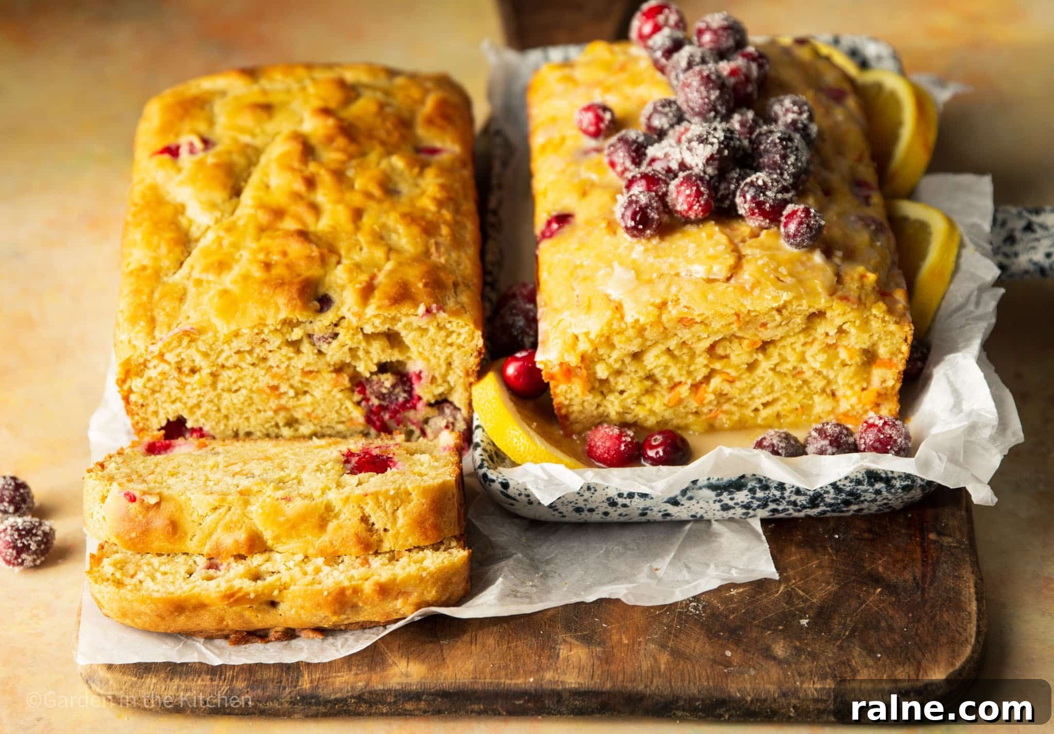 Cranberry Orange Carrot Cake Recipe with Zesty Glaze 8 two cranberry orange carrot cakes next to each other. One being sliced and the other topped with sugared cranberries.