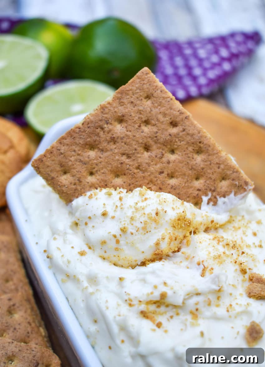 a graham cracker scooping key lime pie dip out of a small white serving dish