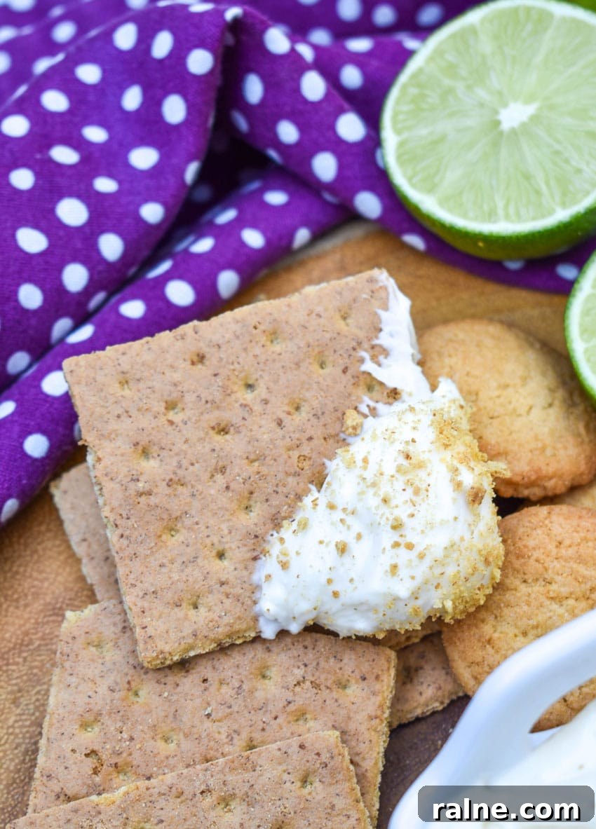 a key lime pie dip topped graham cracker resting on a wooden cutting board