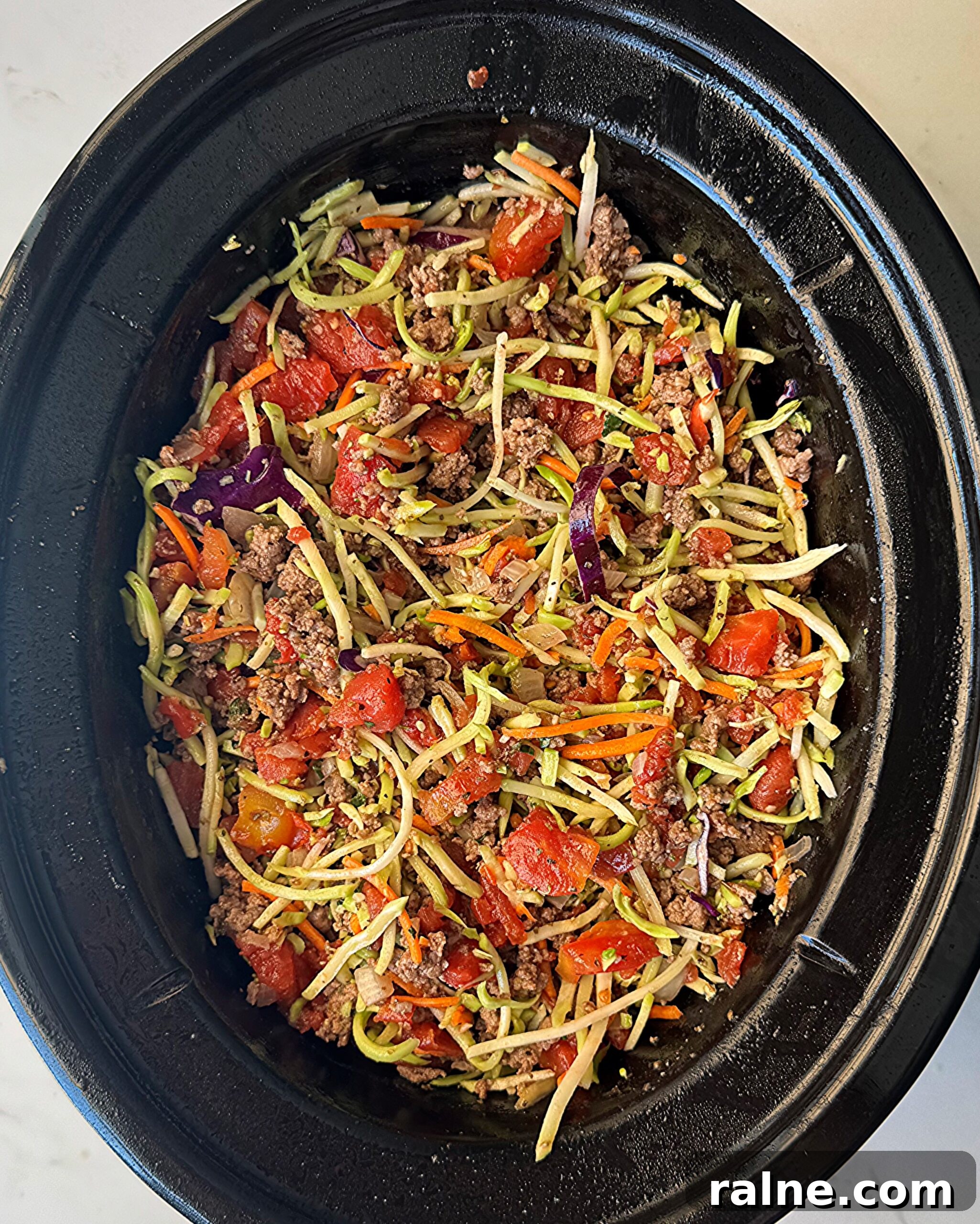 overhead shot of uncooked slawghetti in a black slow cooker