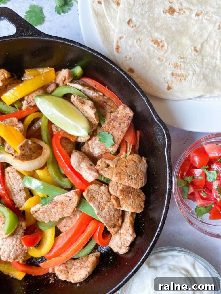 Pork fajitas sliced in a cast iron pan with bell peppers.