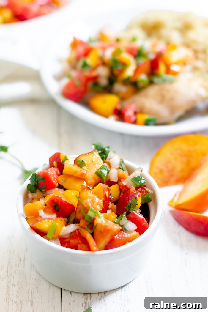 Fresh Peach Salsa Recipe for Grilling, Tacos & Summer Salads 4 Photo shows a bowl of salsa with peaches and tomatoes in front of a plate of chicken with salsa