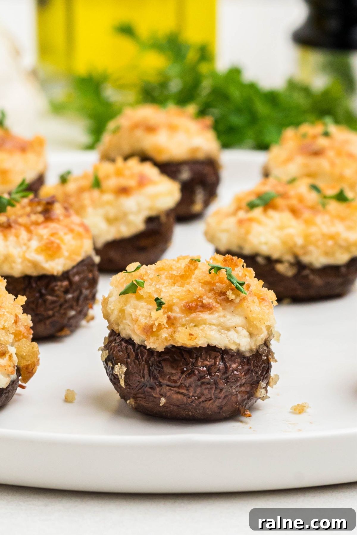 Cheesy Garlic Stuffed Mushrooms with Herb Breadcrumbs 2 Brown mushrooms topped with cream cheese mixture and breadcrumbs, on a white plate.