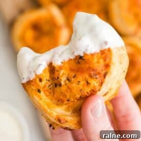 Quick Chicken Dinners for Busy Weeknights 19 A hand holds a partially eaten, saucy, bite-sized buffalo chicken pinwheel with a flaky crust and creamy white dip on top.