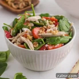 Quick Chicken Dinners for Busy Weeknights 10 A white bowl filled with spinach salad featuring sliced strawberries, shredded chicken, walnuts, and crumbled cheese.