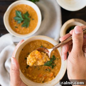 Creamy Coconut Red Lentil Soup with Warm Spices 11 a set of hands holds a spoonful of lentil soup above a white bowl