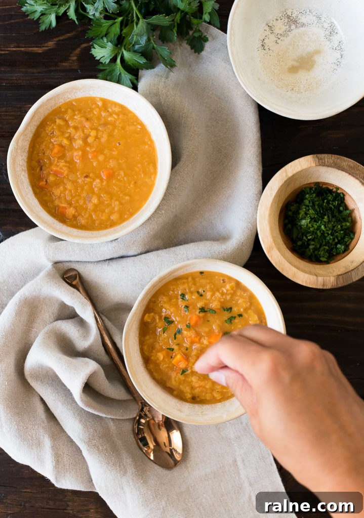 Creamy Coconut Red Lentil Soup with Warm Spices 5 herbs are sprinkled on top of a bowl of lentil soup on a wooden table