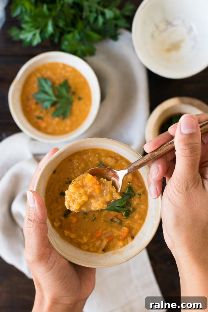 Creamy Coconut Red Lentil Soup with Warm Spices 7 a set of hands holds a spoonful of lentil soup above a white bowl