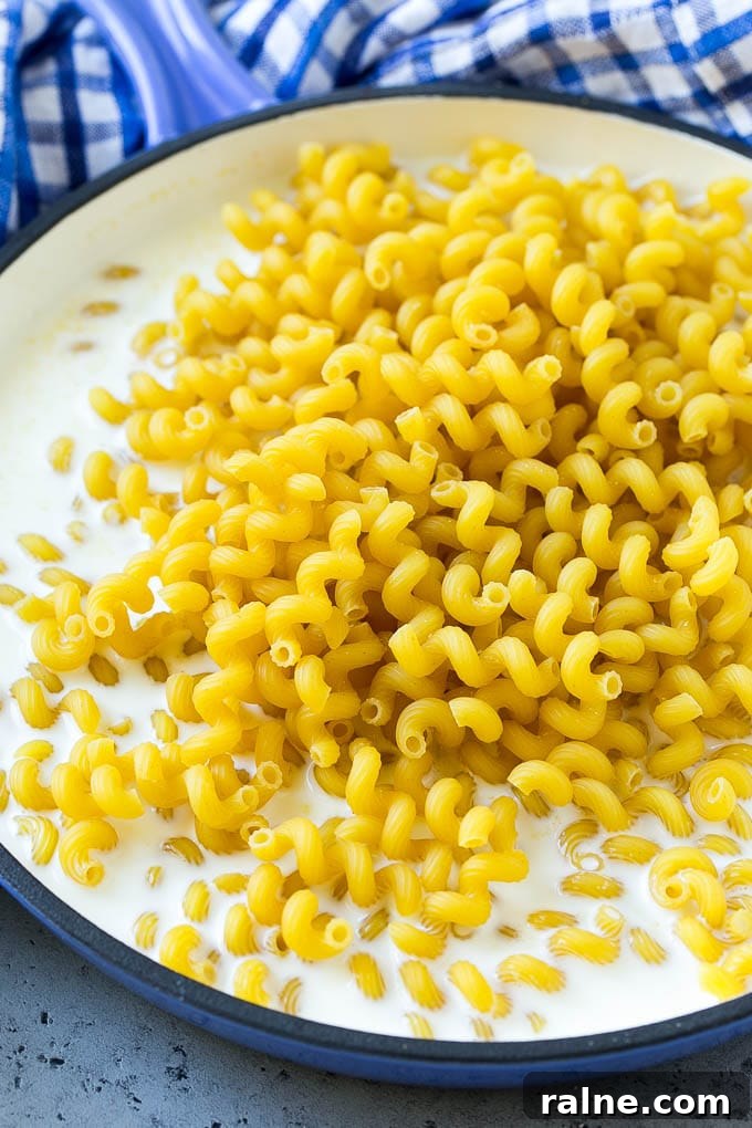 Jalapeño Popper Macaroni and Cheese Recipe 5 Pasta simmering in milk with seasonings in a pan.