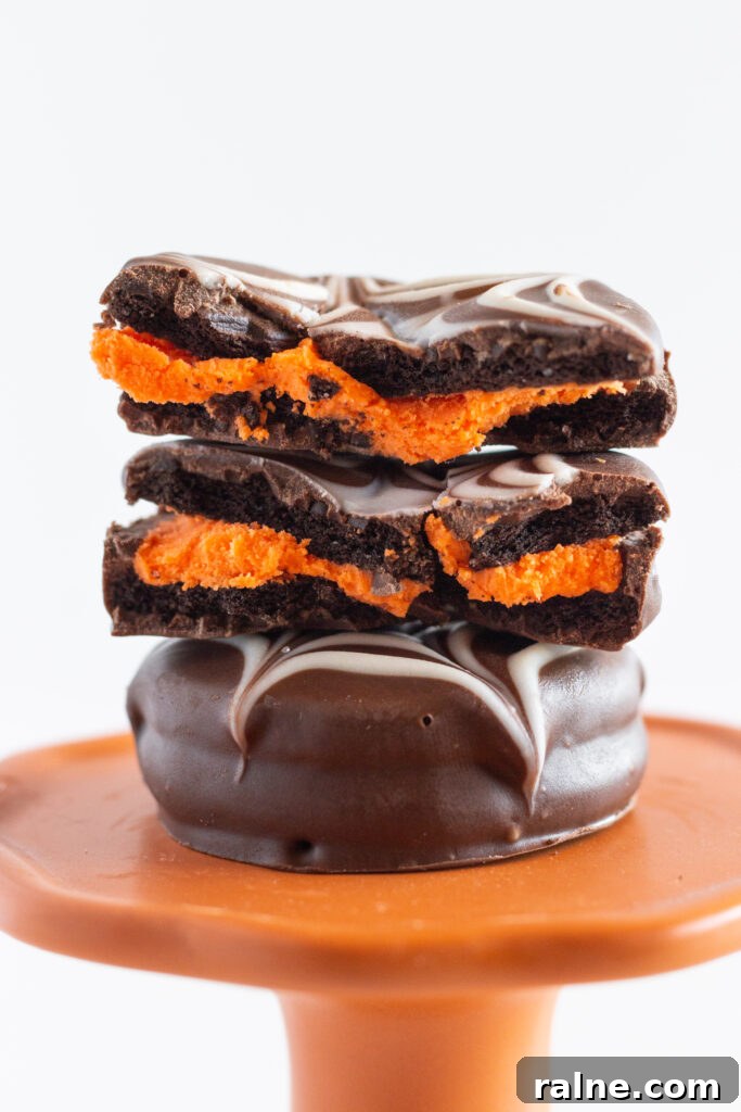 Two Halloween Chocolate Covered Oreos stacked on top of each other. The top cookie is broke into half, so that you can see the orange filling.