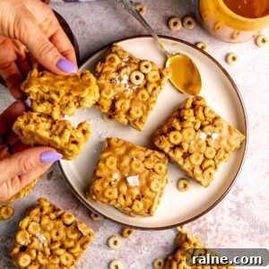 No-Bake Peanut Butter Cheerio Bars Recipe 11 peanut butter and cheerio bars on a white plate with peanut butter on a spoon.