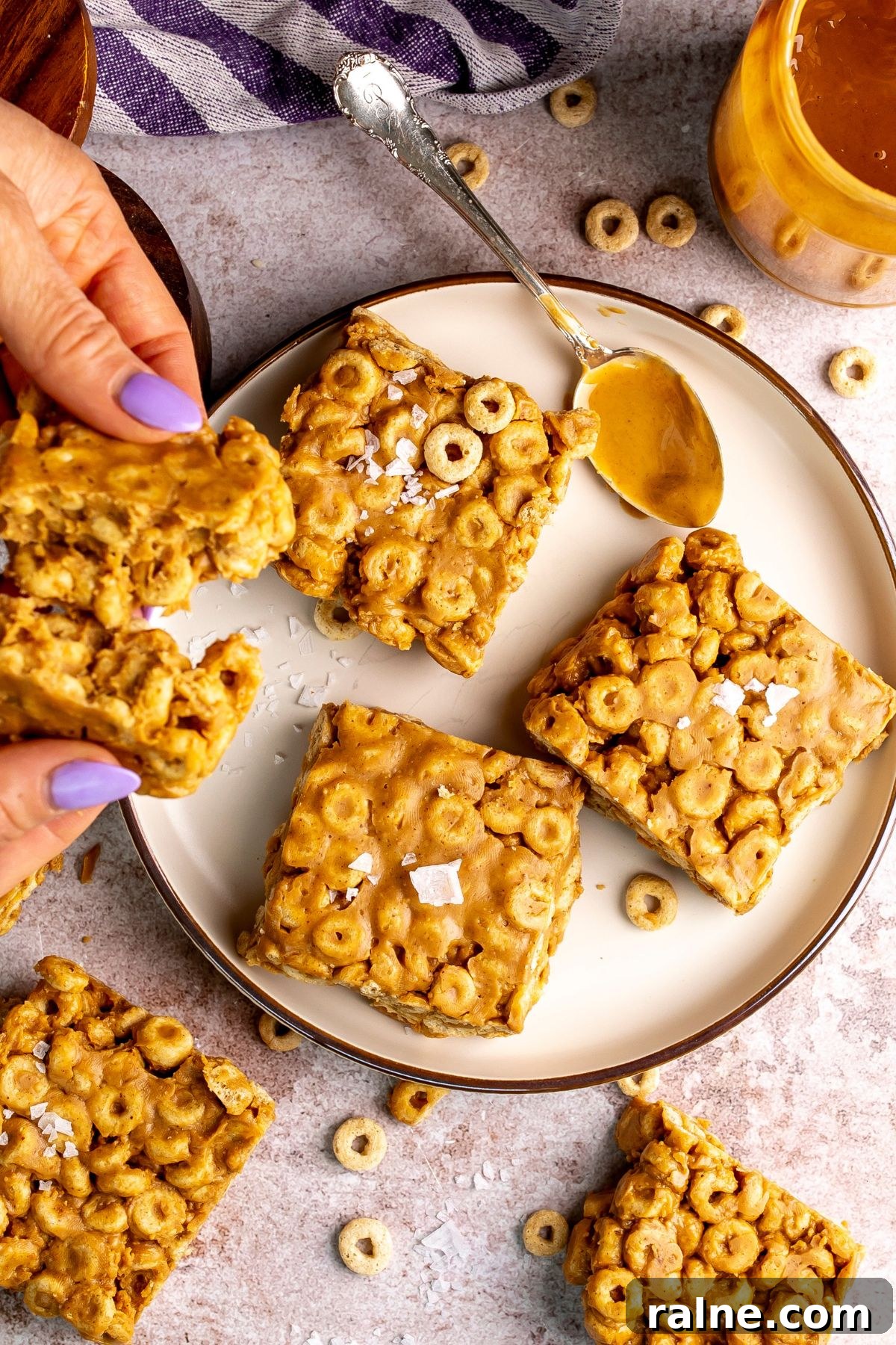No-Bake Peanut Butter Cheerio Bars Recipe 6 peanut butter and cheerio bars on a white plate with peanut butter on a spoon.