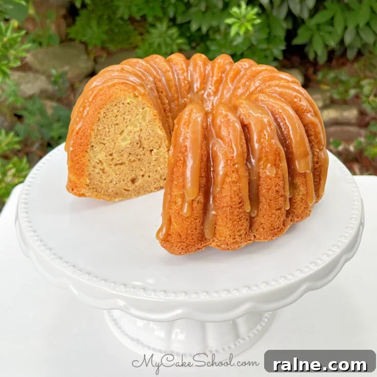 Sliced Apple Bundt Cake on white pedestal, glazed with caramel.