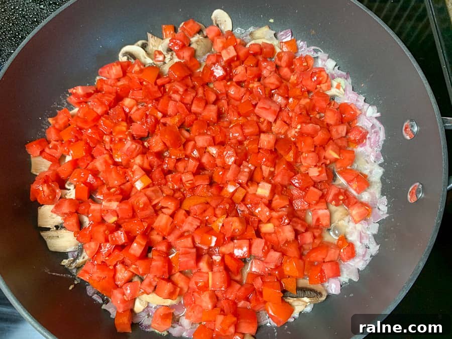Diced roma tomatoes added to mushrooms and onions in a skillet