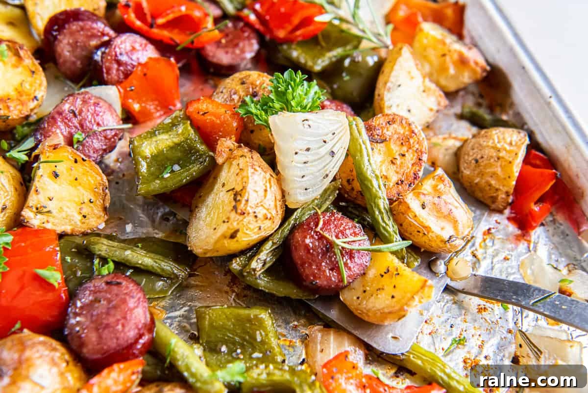A close up of a spatula resting under oven roasted sausage and potatoes on a sheet pan.