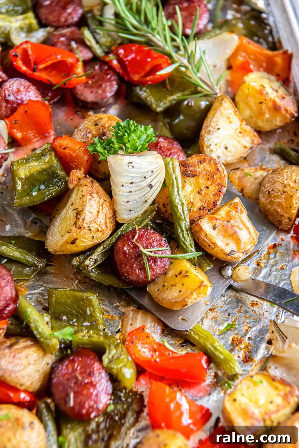 A close up of a spatula resting under oven roasted sausage and potatoes on a sheet pan.