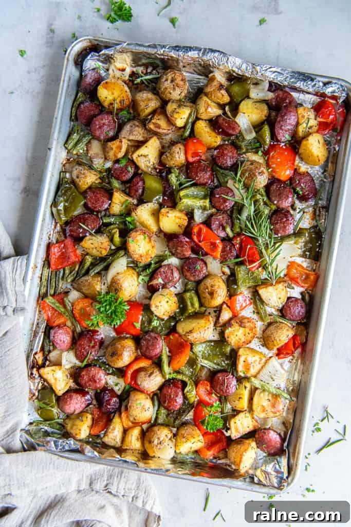 Sausage and potatoes with bell peppers and green beans on a baking sheet.