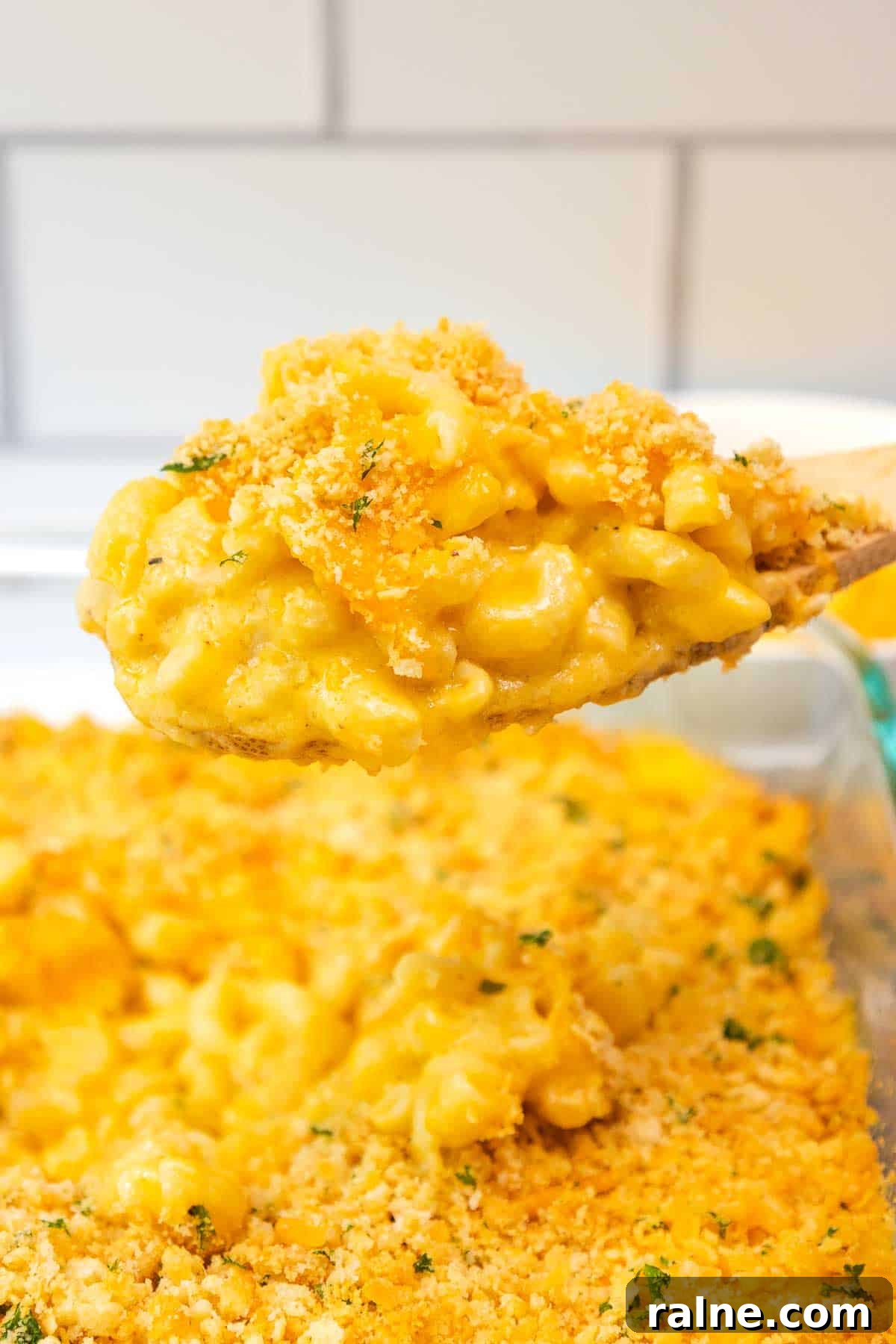 Old-Fashioned Baked Mac and Cheese with Ritz Cracker Topping 2 A wooden spoon lifting a serving of creamy old fashioned baked mac and cheese topped with a golden Ritz cracker crumb crust and sprinkled with parsley.