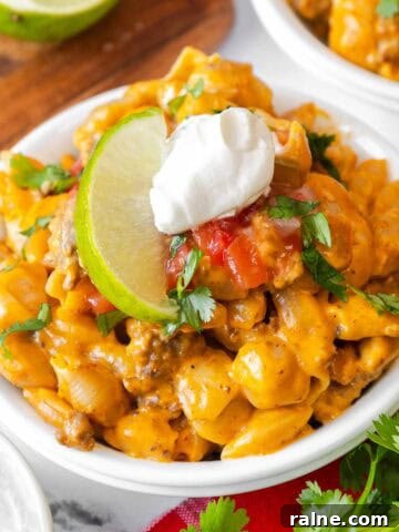 Small white bowl filled with taco mac and cheese, garnished with sour cream, salsa, chopped cilantro, and a lime slice.
